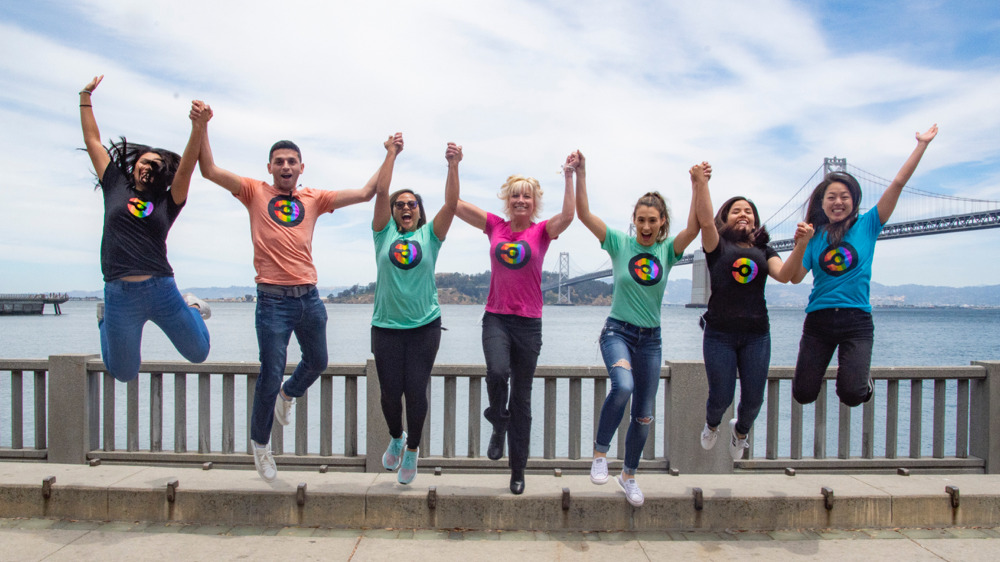 Team members in CircleCI branded t-shirts jumping in the air outside in front of the Bay Bridge in San Francisco.