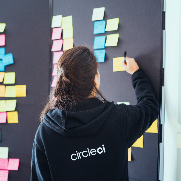 Team member writing on a sticky note on a board with many sticky notes on it. She’s wearing a CircleCI branded sweatshirt.
