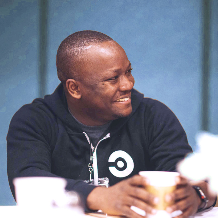 A team member smiling, with a cup of coffee in his hands.